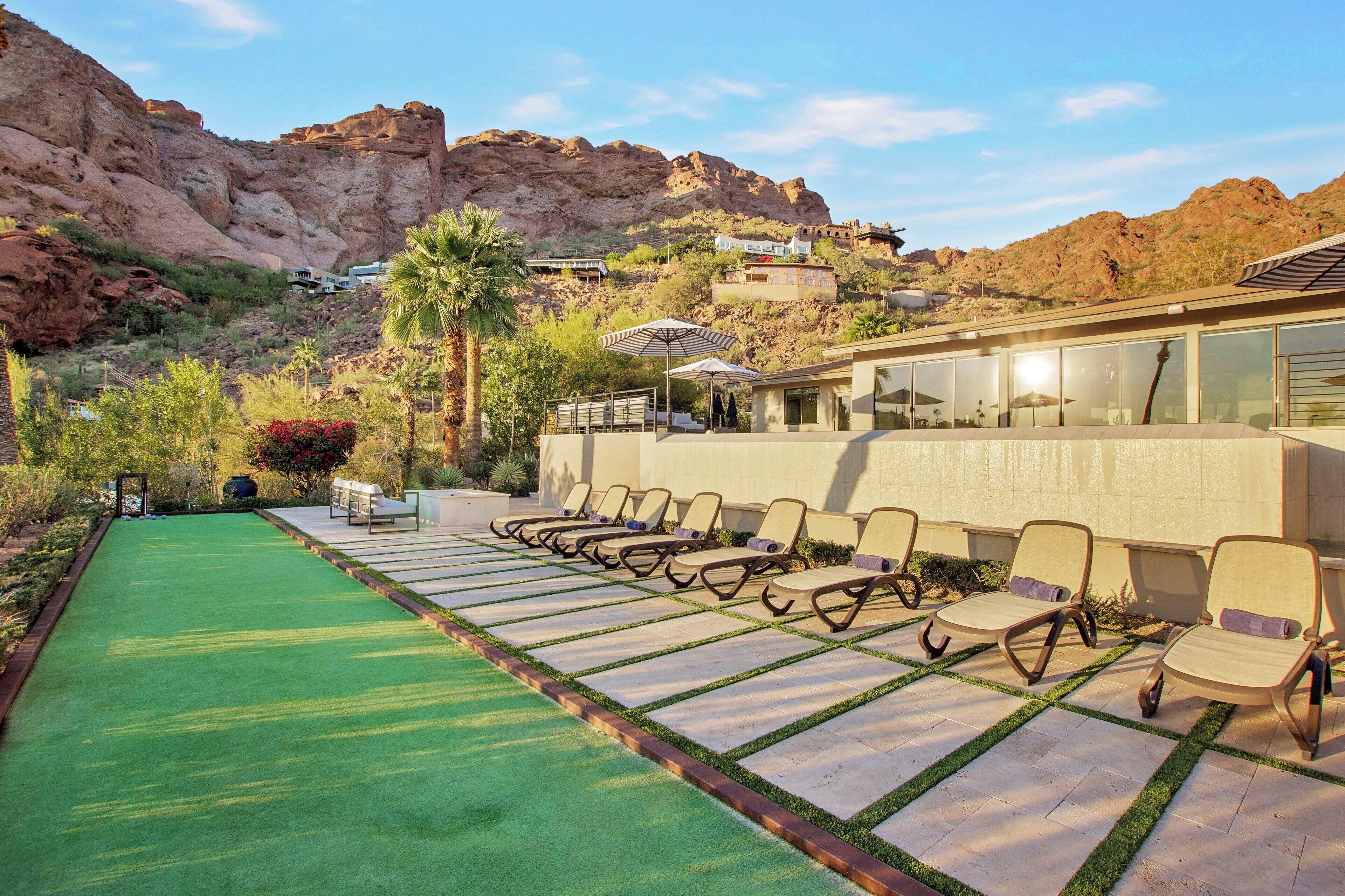 Un espace piscine doté de chaises longues et d’une pelouse artificielle verdoyante, entouré d’une végétation désertique et avec des montagnes en toile de fond.
