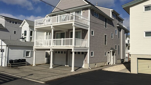 A two-story residential building with a balcony on the second floor, a garage, and a driveway.