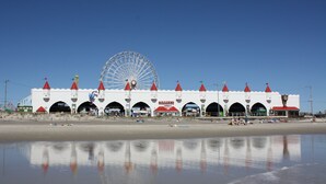 A coastal building with multiple arched entrances, a large Ferris wheel in the background, and a beach in the foreground.