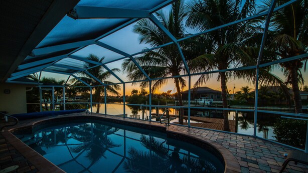 An indoor swimming pool with a view of palm trees and a sunset. - Fun for the Whole Family! Pool Table, Heated Pool, Fishing Dock -Villa Serendipity-Roelens Vacations (Cape Coral)