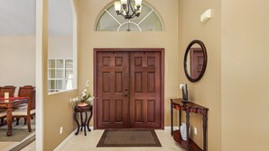 A hallway with a double wooden door, a small table with a vase, a mirror, and a chandelier. - Fun for the Whole Family! Pool Table, Heated Pool, Fishing Dock -Villa Serendipity-Roelens Vacations (Cape Coral)
