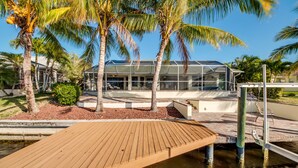 A modern building with a glass facade, surrounded by palm trees and a wooden deck over water. - Fun for the Whole Family! Pool Table, Heated Pool, Fishing Dock -Villa Serendipity-Roelens Vacations (Cape Coral)