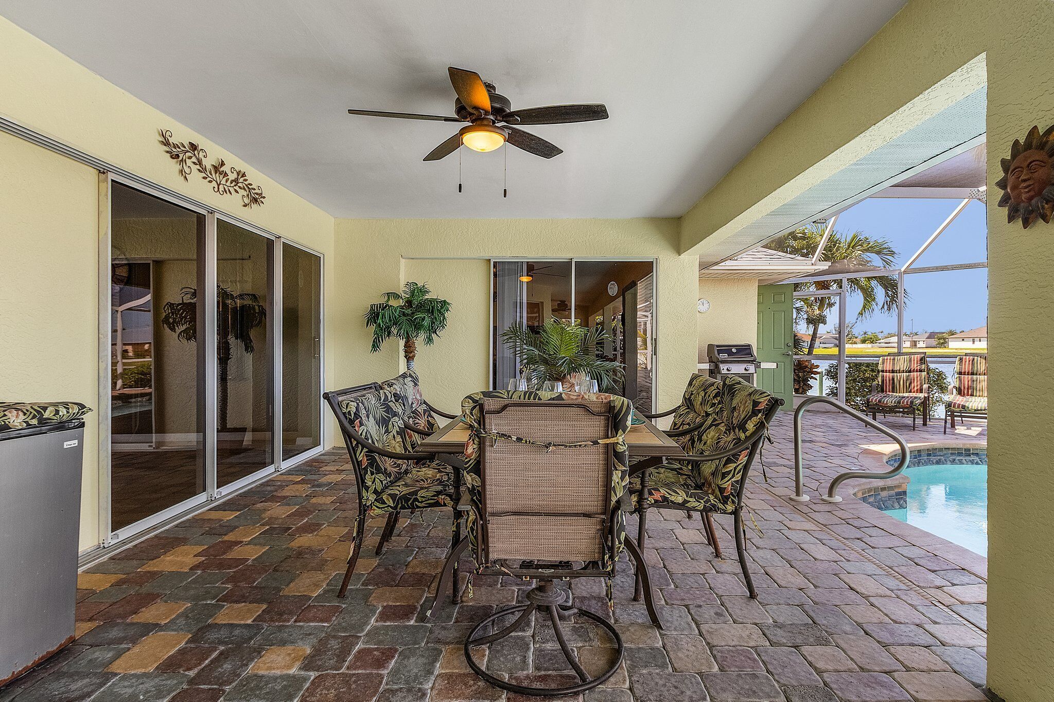 A covered outdoor area with a pool, a ceiling fan, and a table with chairs.