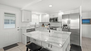 A modern kitchen with white cabinetry, a central island, stainless steel appliances, and a window with blinds.