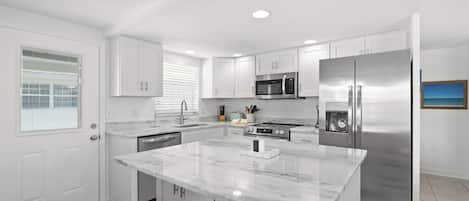 A modern kitchen with white cabinetry, a central island, stainless steel appliances, and a window with blinds.