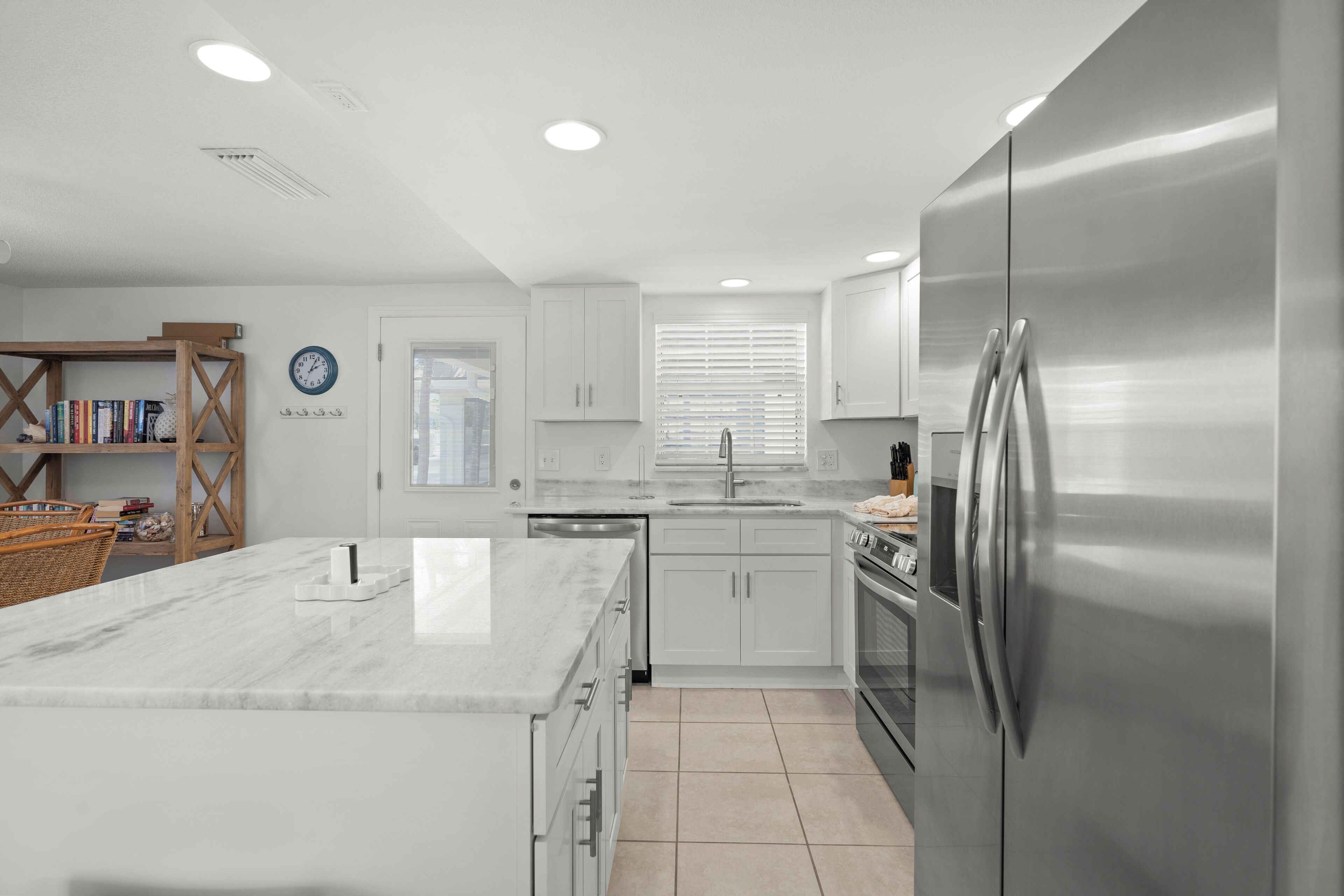 A modern kitchen with white cabinetry, a stainless steel refrigerator, and a marble countertop.