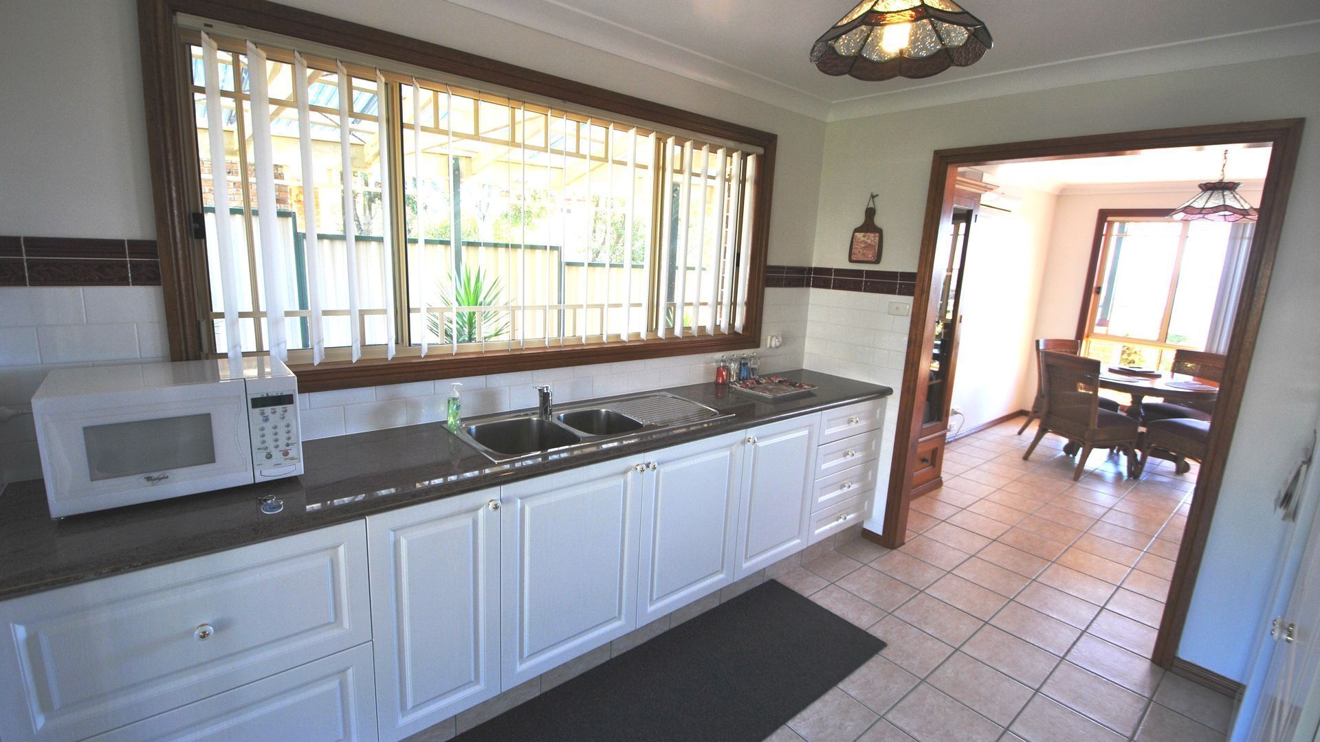 A kitchen with white cabinets, a black countertop, a microwave, a sink, and a window with blinds.