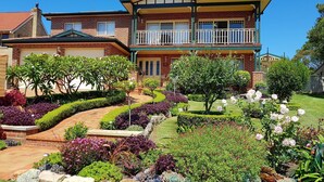 A two-story house with a balcony, surrounded by well-maintained gardens and a clear blue sky. - Best views of Jervis Bay, A/C,heating, free Internet & beautiful large apartment (Vincentia)