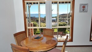 A dining area with a round table, four chairs, and a view of a residential neighborhood through large windows. - Best views of Jervis Bay, A/C,heating, free Internet & beautiful large apartment (Vincentia)