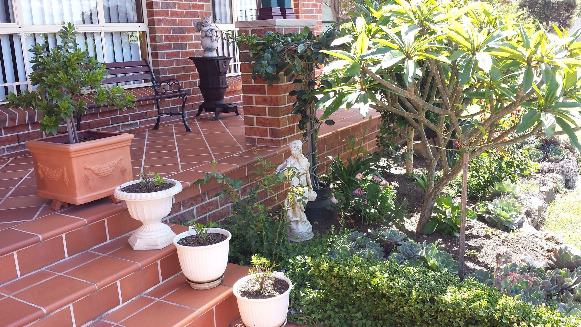 Un patio de ladrillo con plantas en macetas y una estatua.
