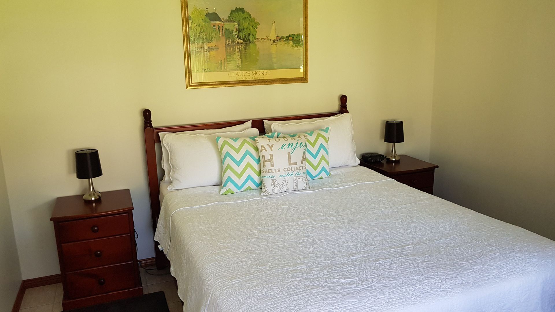 A neatly made bed with a white quilt, two nightstands with lamps, and a framed painting above the bed.
