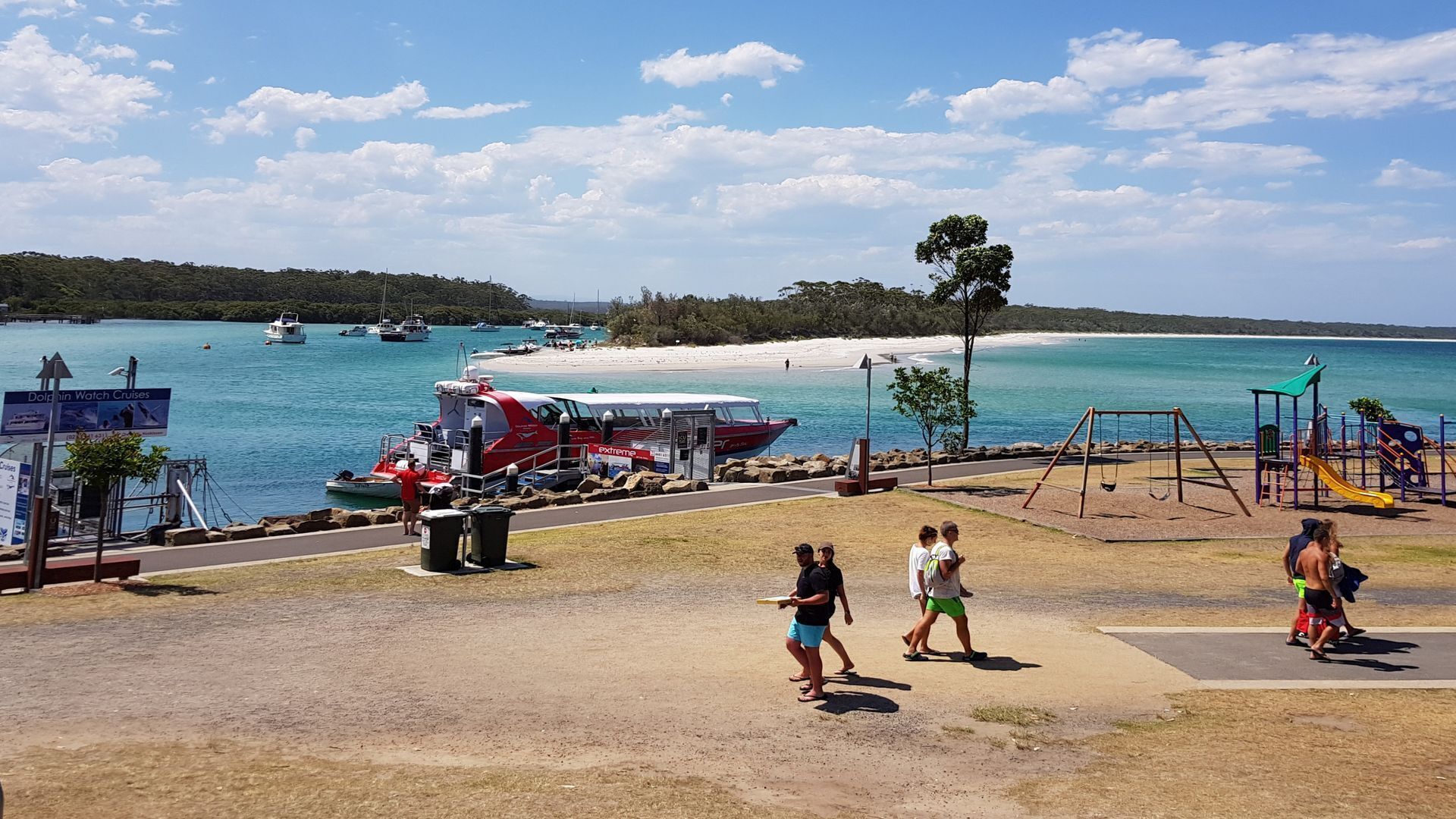 A coastal park with a playground, a boat dock, and a clear view of the beach and ocean.