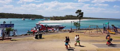 A coastal park with a playground, a boat dock, and a clear view of the beach and ocean.