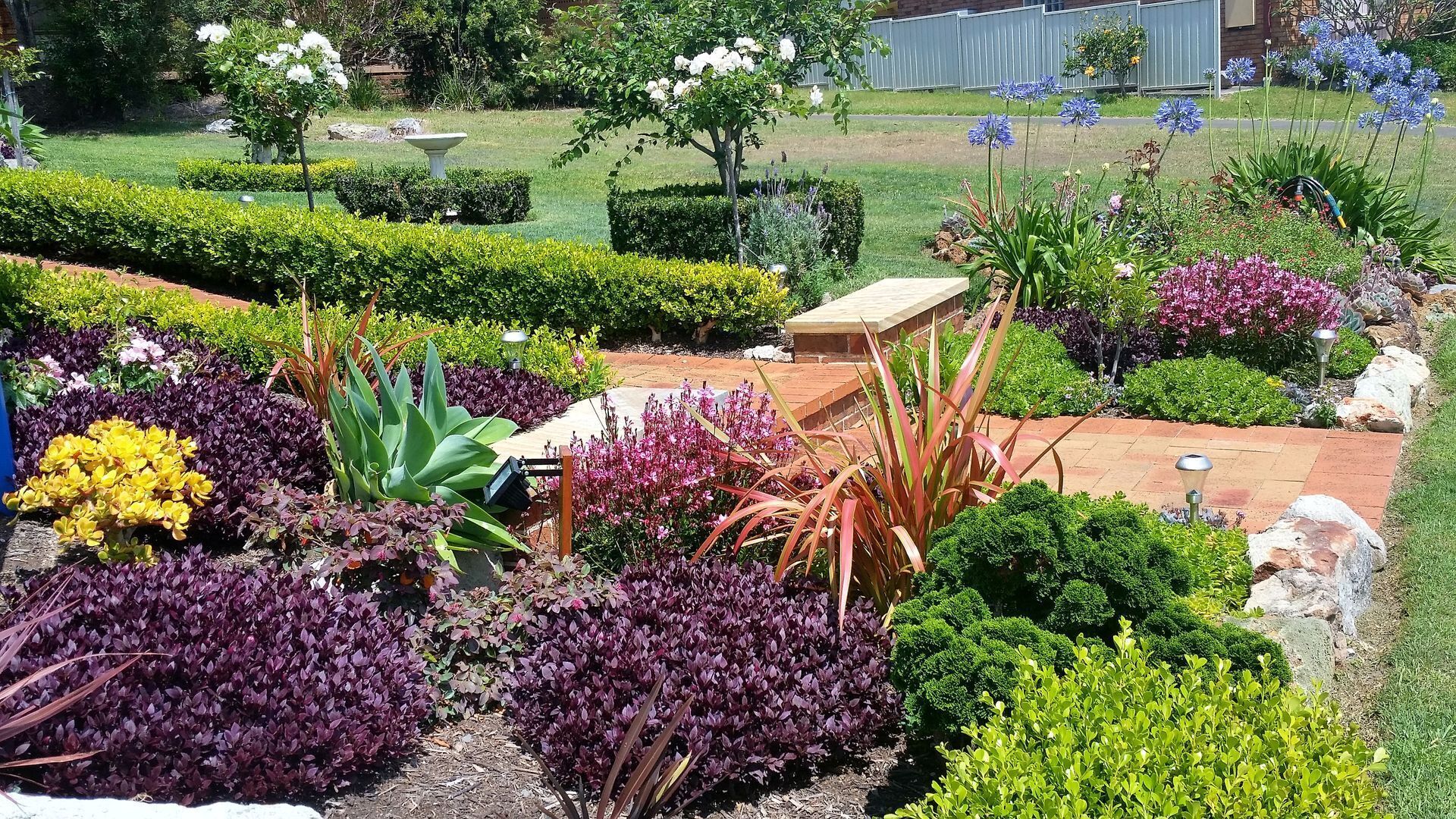 Un jardín bien cuidado con diversas plantas y un banco de piedra.