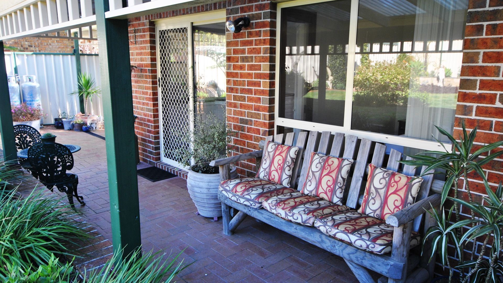 Une terrasse couverte avec un banc en bois et des plantes en pot.