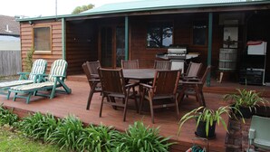 Eine Holzterrasse mit Tisch, Stühlen, einem Grill und einem kleinen Schuppen.