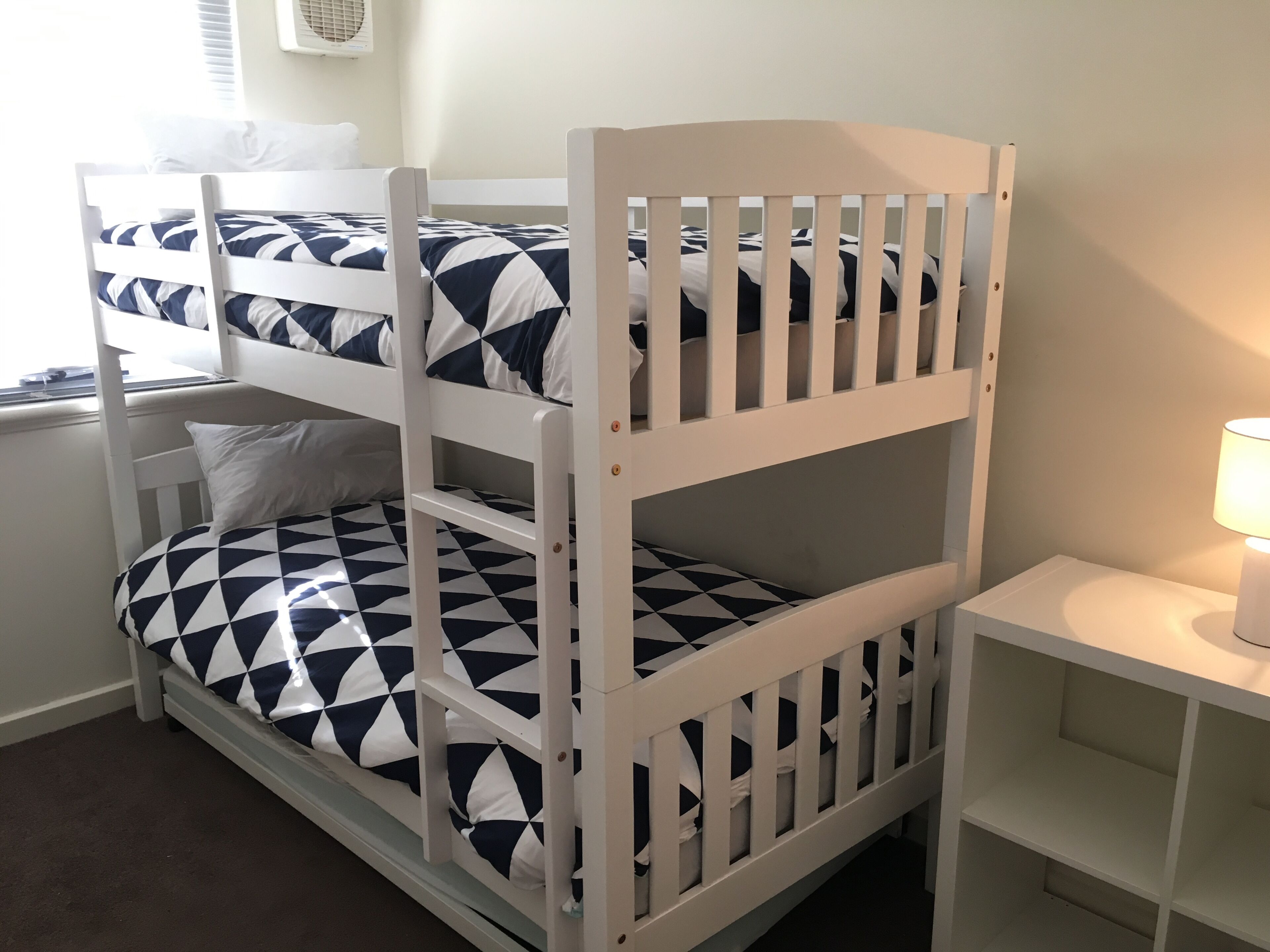 A bunk bed with a geometric-patterned mattress, a bedside table with a lamp, and a window with blinds.
