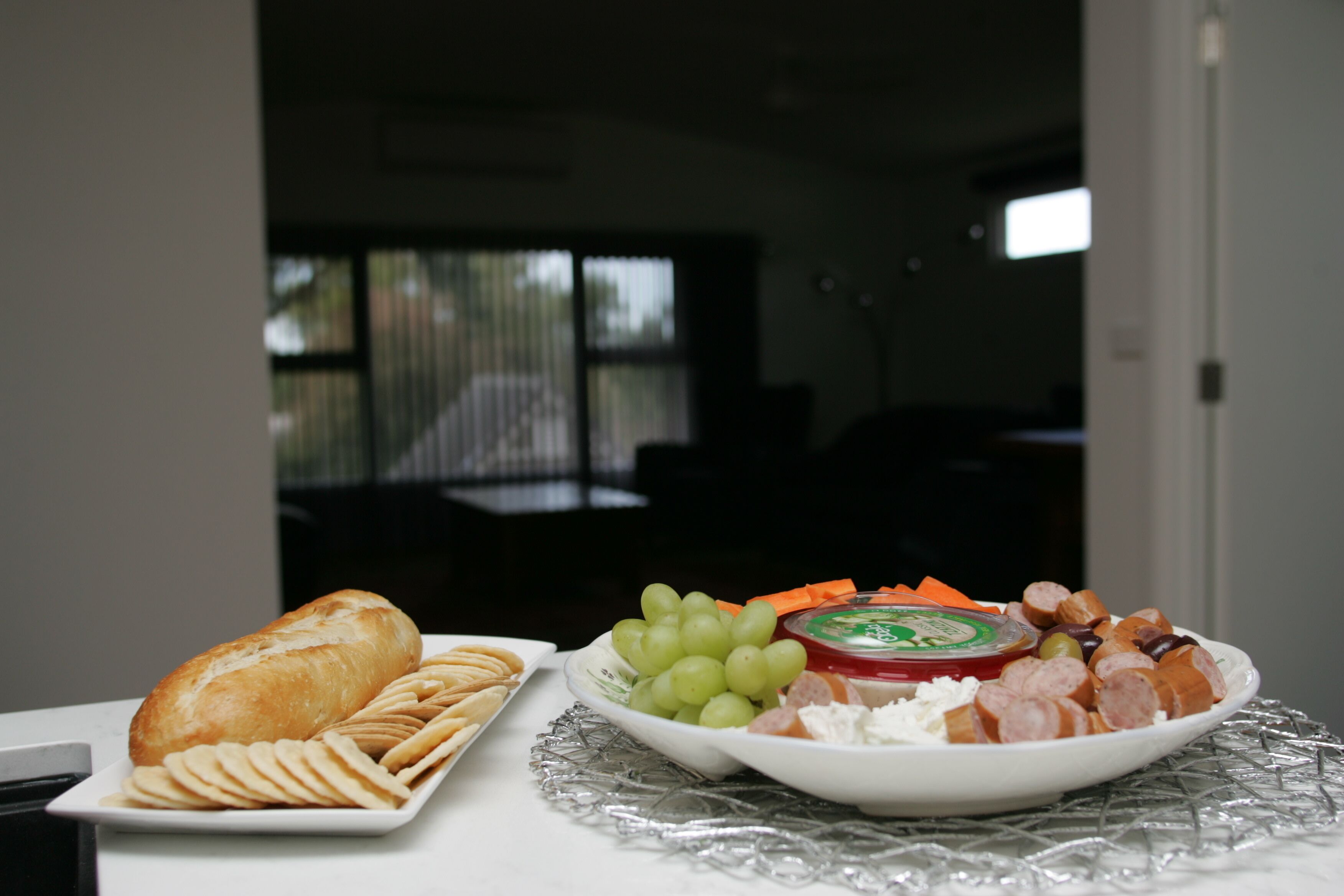 Ein Tisch mit einer Platte, belegt mit Brot, Crackern, Trauben, Käse und verschiedenen Fleischsorten.