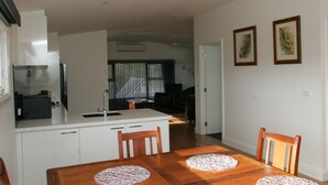 Une cuisine moderne avec des meubles blancs, une table à manger en bois agrémentée de sets de table, et une vue sur le salon.