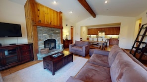 A living room with a stone fireplace, wooden beams, a television, and a sofa.