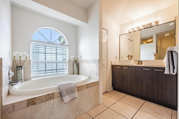 Un baño moderno con una bañera independiente, un espejo grande y una ventana con persianas.