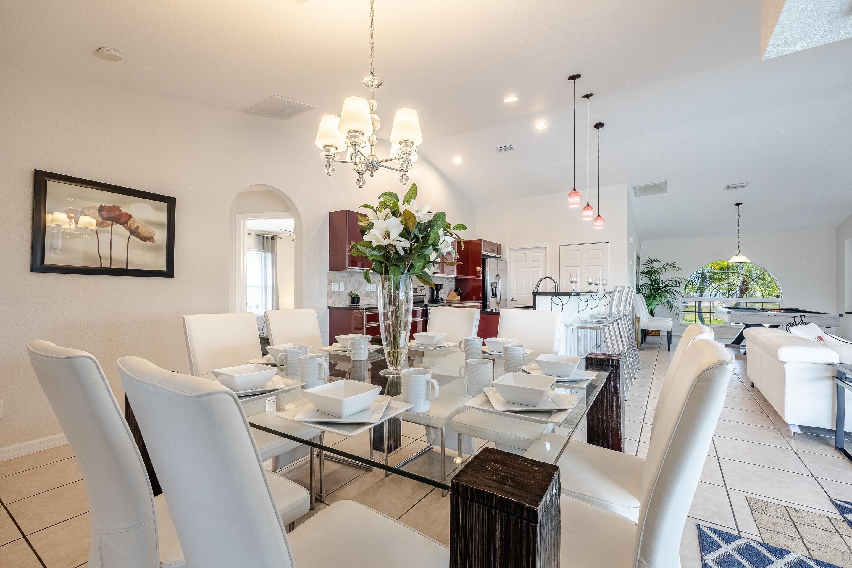 Un espace repas moderne avec une table en verre, des chaises blanches et un vase de fleurs.