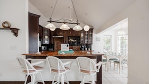 Cozinha com ilha central, banquetas, armários de madeira escura e iluminação pendente.