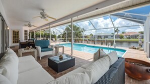 Ampla área de pátio com piscina, móveis de exterior e vista para um lago e edifícios.