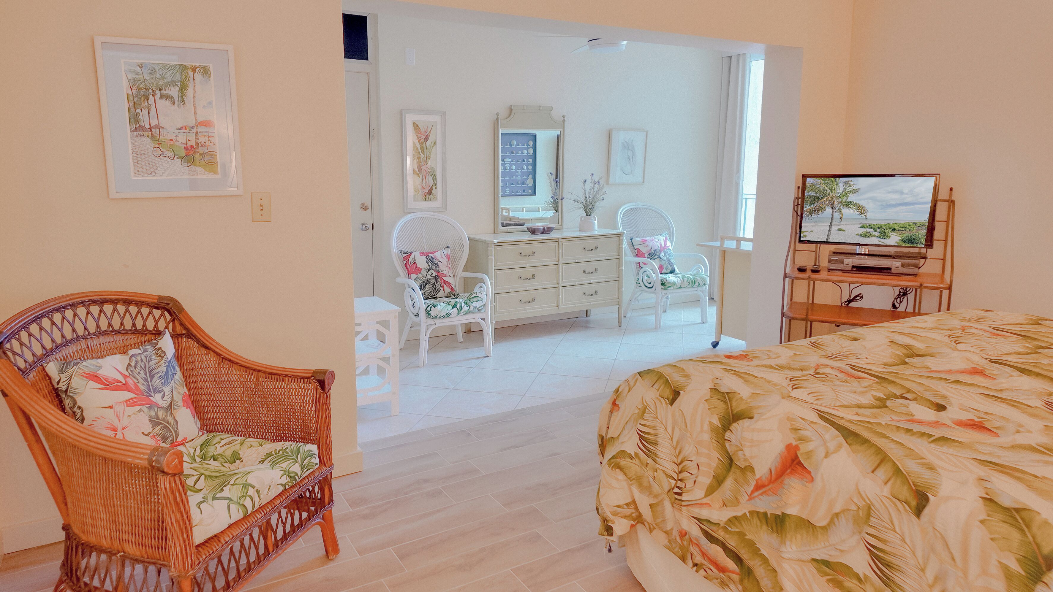 A bedroom with a bed, a wicker chair, a dresser, and a television.