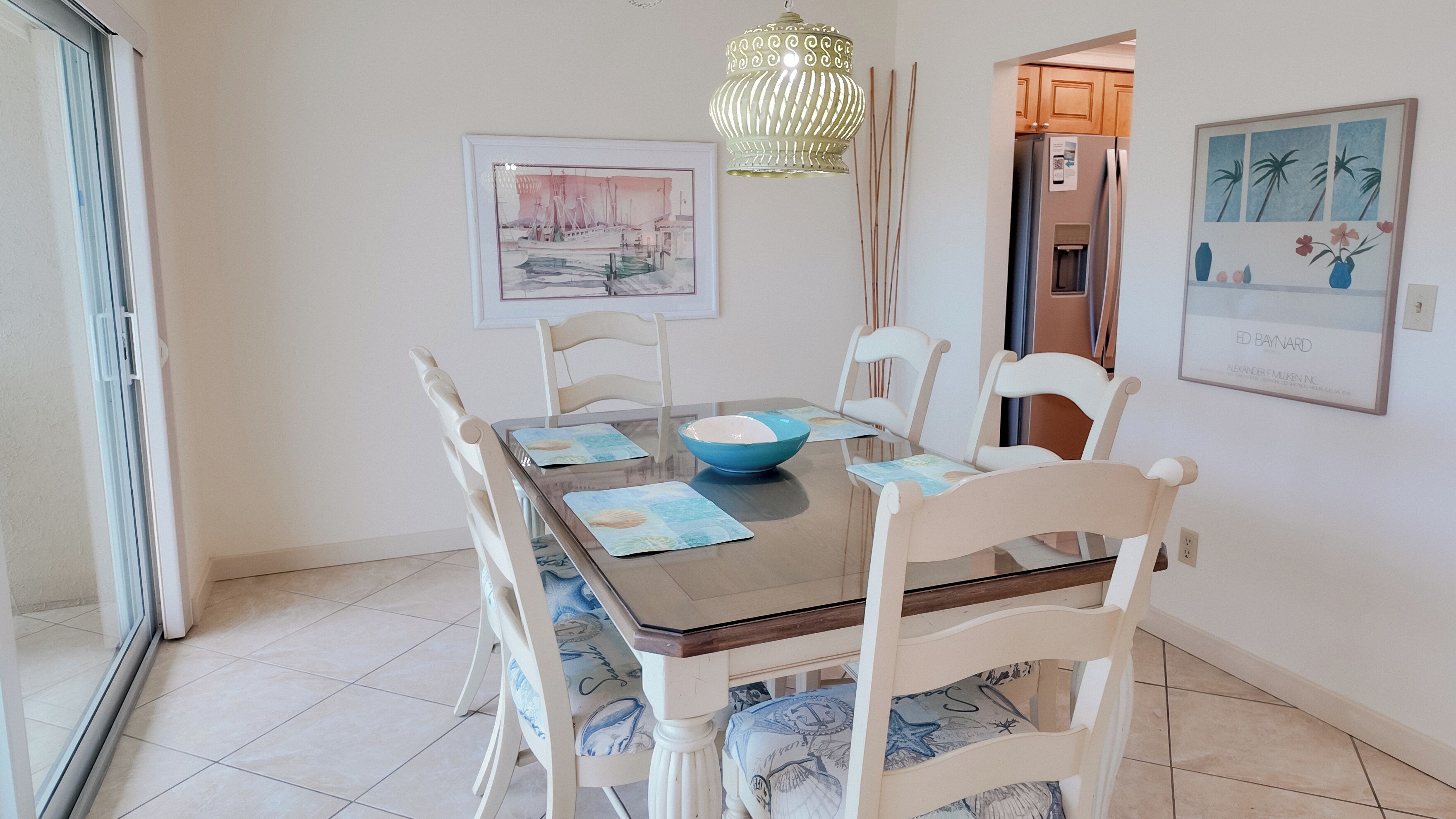 A dining area with a glass table, white chairs, a blue bowl, and a framed picture on the wall.