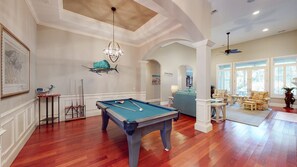 A spacious room with a pool table, a ceiling fan, and a seating area with a view of the outdoors.