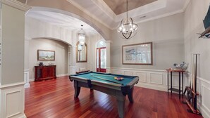 A spacious room with a pool table, wooden flooring, and a chandelier. - No Expense Spared - This Home is Perfect! (Hilton Head)
