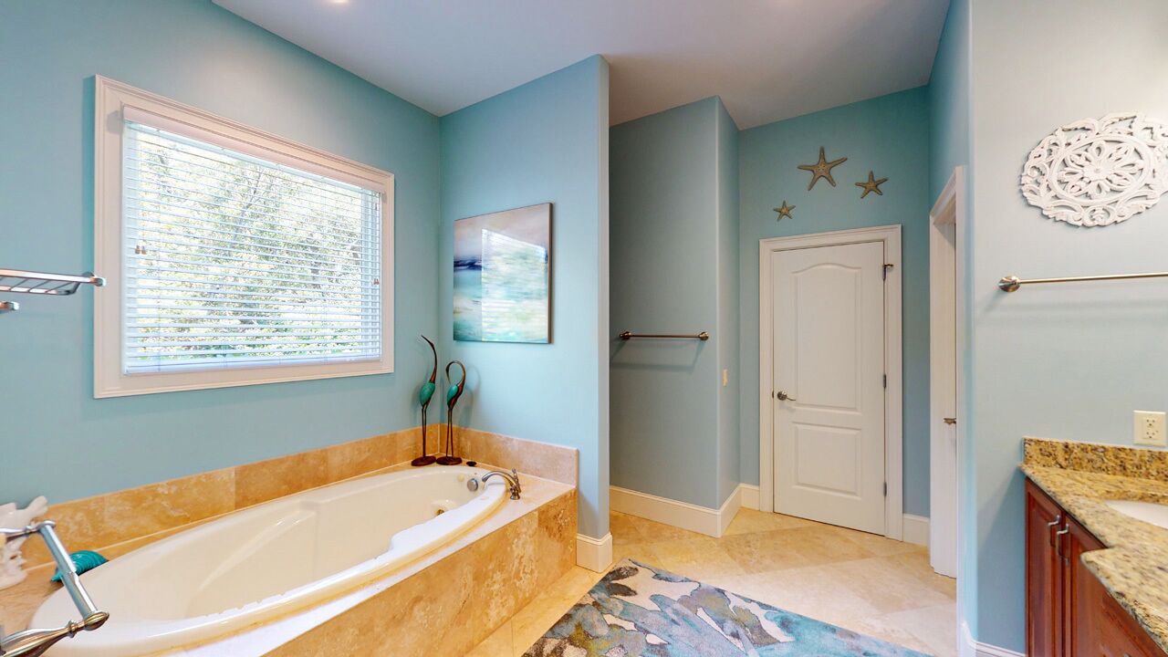 A bathroom with a bathtub, a window with blinds, a door, and a towel rack.