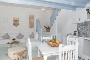 A modern kitchen with white cabinets, a dining table with a fruit basket, and a staircase leading to an upper level. - Rafaela Apartments (Patmos)