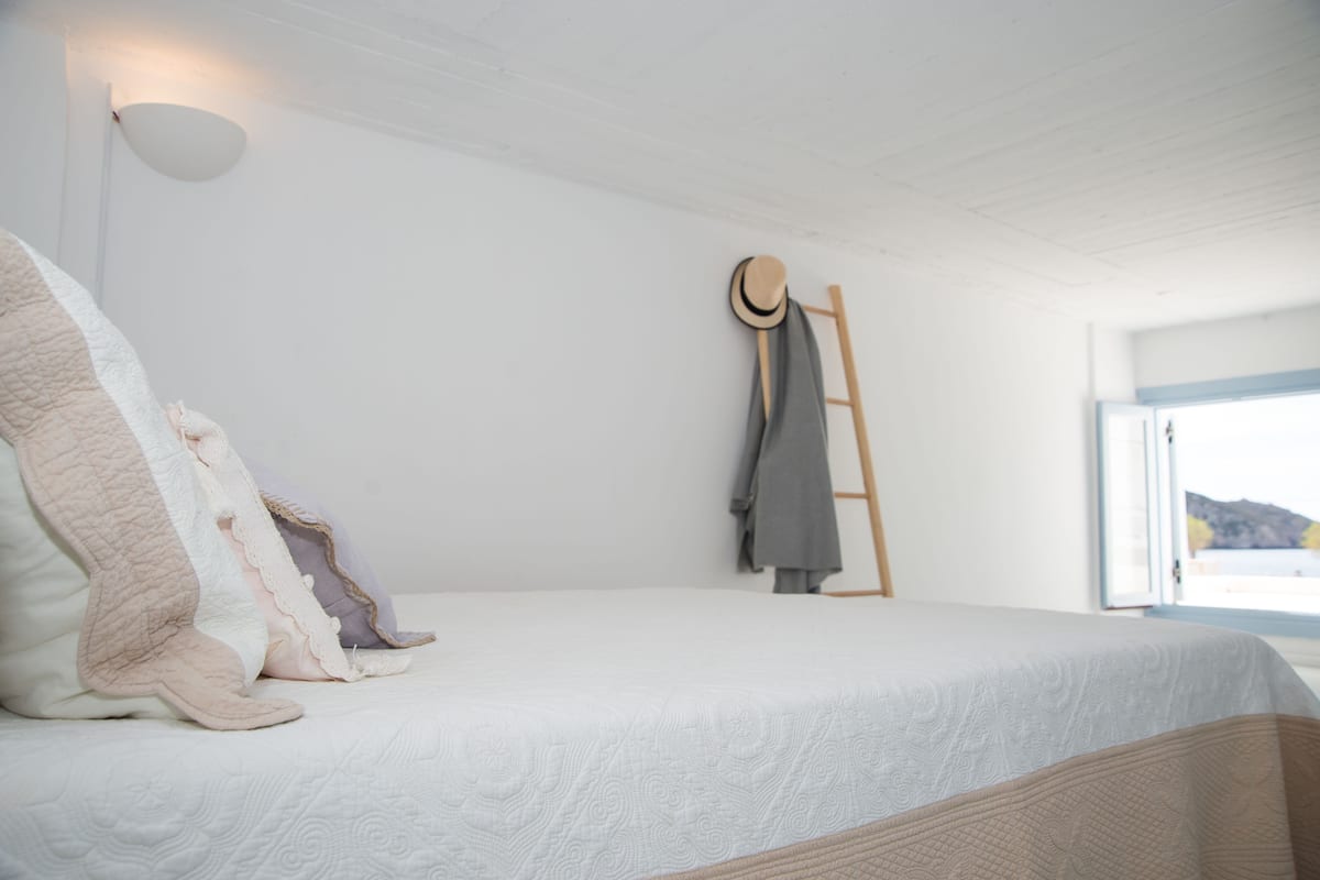 A bedroom with a bed, pillows, a hat on a wall-mounted rack, and a window with a view.