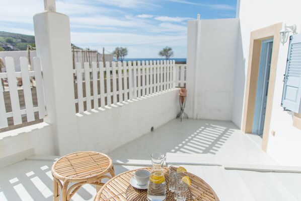 A balcony with two wicker chairs, a table with a bottle and glasses, and a white fence.