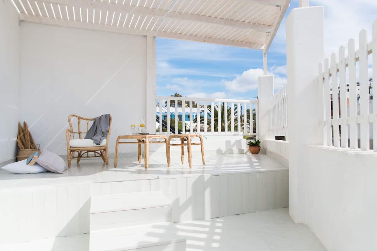 A white outdoor patio with wicker furniture, a potted plant, and a view of the sky and buildings.