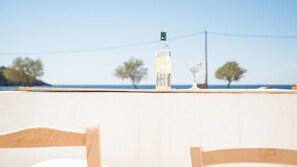 A table with a bottle and a glass, overlooking a clear blue sky and distant trees.