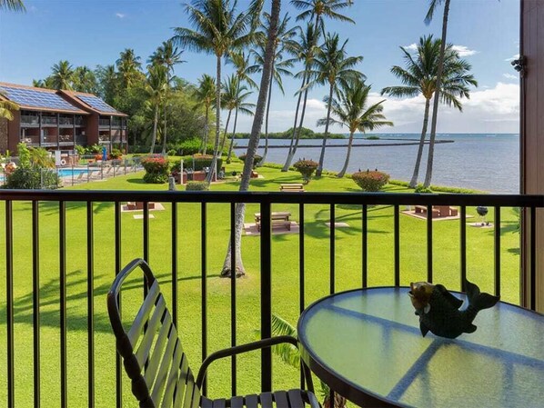 A balcony with a view of a pool, palm trees, and a building with solar panels. - Modern Hawaii Style w/Kitchen, WiFi, Lanai–#205 (KAUNAKAKAI)