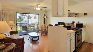 A compact living space with a kitchenette, dining area, and a balcony with a view of palm trees. - Tropical Style w/OF Lanai, Flat Screen, WiFi–#229 (KAUNAKAKAI)