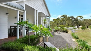 A white building with a covered outdoor area, gravel pathway, and various plants.