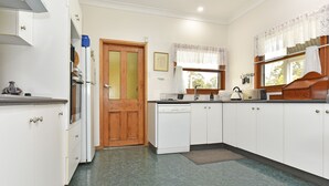 A compact kitchen with white cabinets, a wooden door, a window with lace curtains, and a tiled floor.