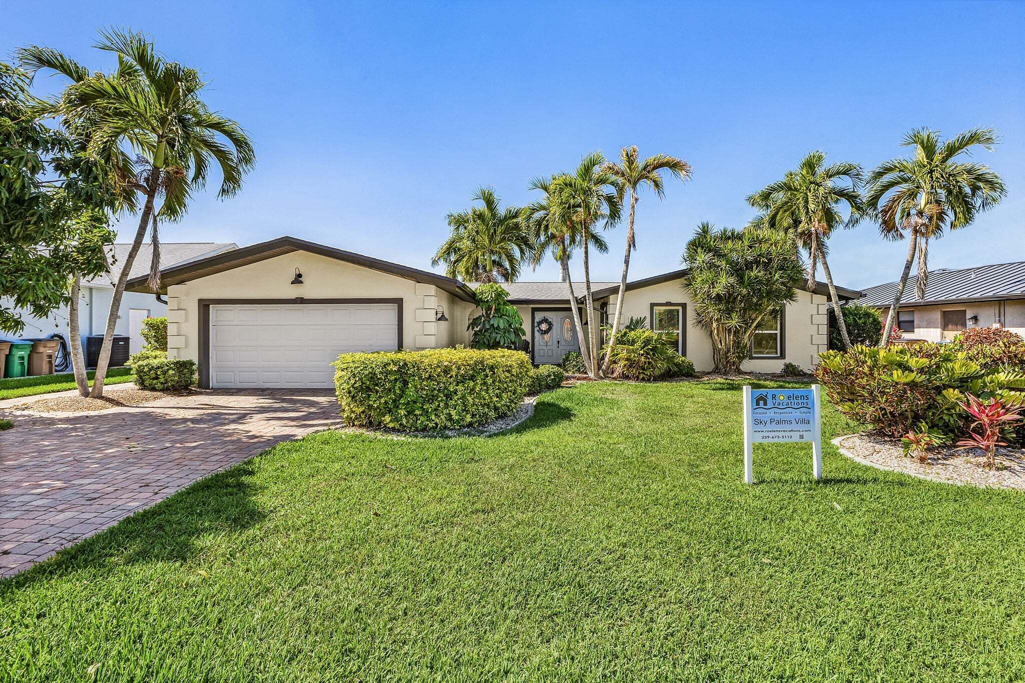 A residential property with a garage, palm trees, and a sign indicating it's a rental.