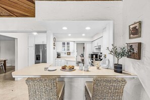 Een moderne keuken met witte kasten, een centraal eiland en een eethoek met rieten stoelen.