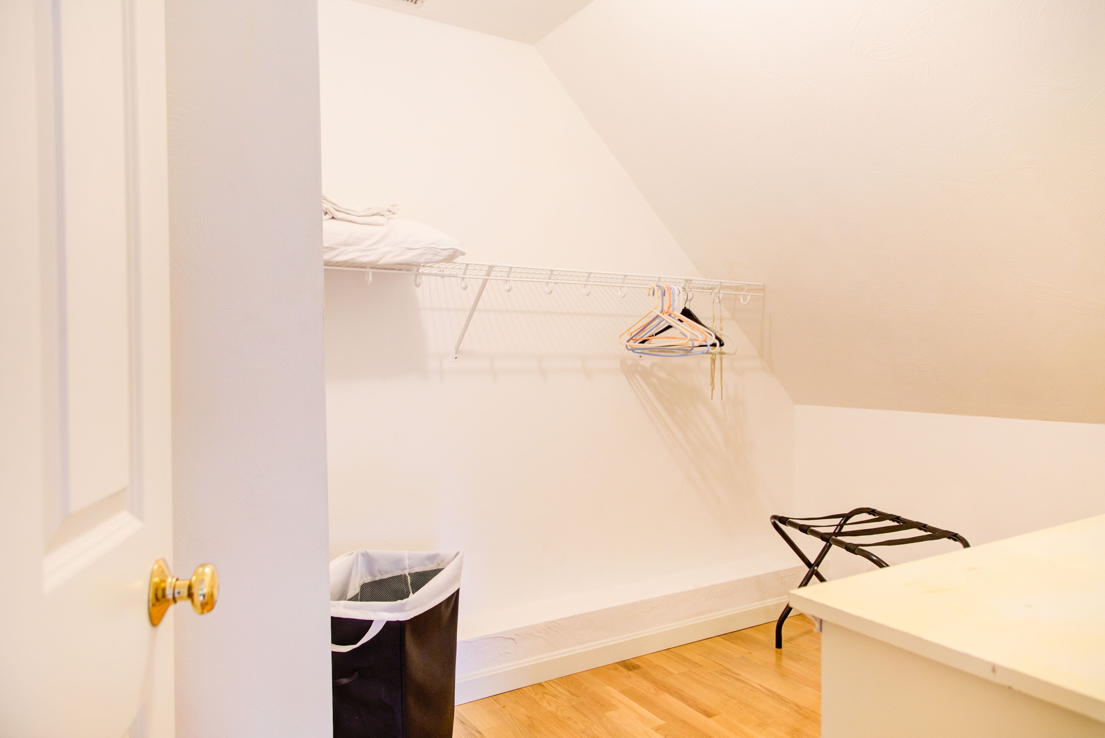 Une pièce avec un plancher en bois, un mur blanc, un étendoir à linge en métal et une chaise noire.