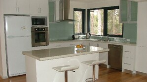 A modern kitchen with a central island, stainless steel appliances, and a view of the outdoors through large windows. - Braidwood Escape Denmark (Denmark)