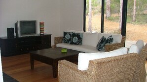 A living room with a sofa, coffee table, TV, and a view of trees. - Braidwood Escape Denmark (Denmark)