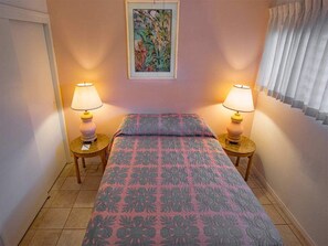 Een slaapkamer met een bed, twee bedlampen, een lijst met een foto aan de muur en een raam met gordijnen.