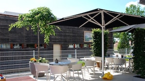 An outdoor patio with white chairs and tables, a large umbrella, and potted plants. - Schlafzimmer Hotel (Dinkelsbuehl)