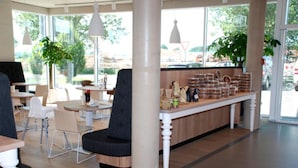 A modern cafe with a long counter, seating area, and large windows. - Schlafzimmer Hotel (Dinkelsbuehl)